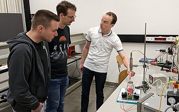 Tim Geboers (right), a student at Hasselt University, explains to two fellow students how to set up the 3D-printed microfluidic system he designed using the experimental setup he created as part of his Master's thesis at HSKL.