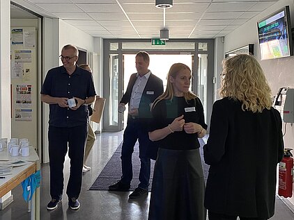 Einlass zum Tag der Lehre: Mehrere Menschen stehen vor dem Tisch der Anmeldung, manche mit einer Tasse als Give-Away in der Hand