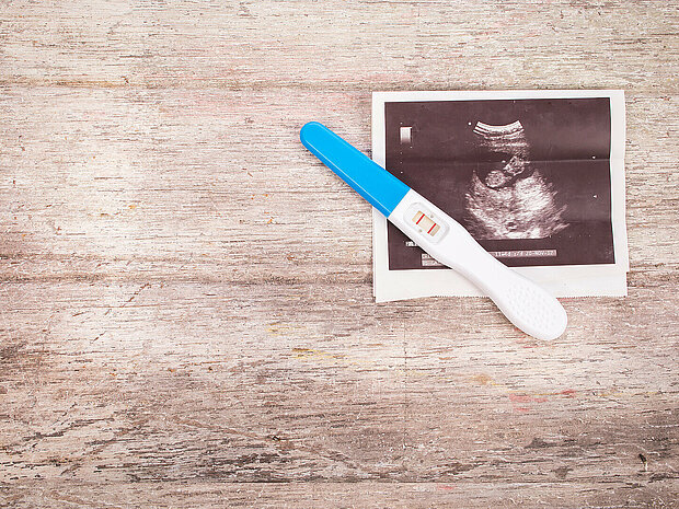 positiver Schwangerschaftstest mit Ultraschallbild auf hölzernem Untergrund